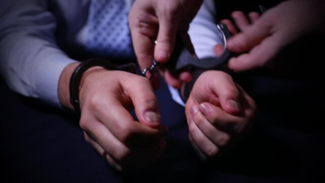 arrest of a criminal.
Arrest of the offender without resistance. Policeman puts the handcuffs on the hands of criminal, hands closeup. Detention of the accused business person.