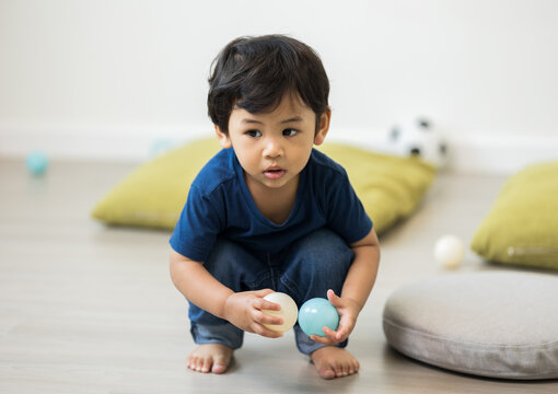 An Asian boy about 1 year old. Play in the living room of the house. He is wearing a blue shirt.