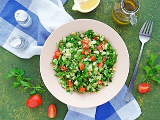 Tabbouleh, parsley, tomato and cucumber vegetable salad with bulgur in a clay plate on an olive concrete background. Salad recipes. Healthly food.