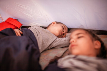 Kids sleeping in the camping tent during family local getaway. Children in the sunrise light, overnight in the wild nature. Healthy lifestyle, green local tourism and vacations, campsite. Soft focus