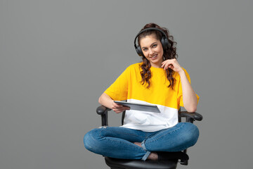 Fototapeta na wymiar teenager with long wavy hair dressed in a yellow t-shirt sitting on an office chair and using tablet