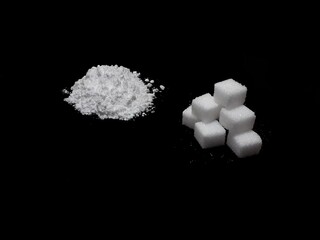 Cocaine drug powder pile and ump sugar cubes on black background, sugar is more addictive than cocaine, isolated cubes of white sugar and cocaine on black background