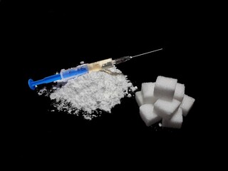 Injection syringe on cocaine drug powder pile and lump sugar cubes on black background, sugar is...