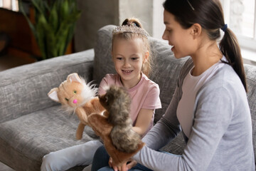 Happy mum and excited daughter girl wearing princess tiara talk play toy fluffy hand puppets together at home. Mother or nanny entertains preschool kid with role game activity. Family, daycare concept