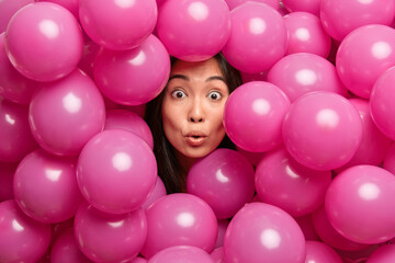 Fototapeta na wymiar Surprised brunette birthday girl stares with eyes popped out keeps head through inflated balloons in one color cannot believe in something awesome preapres for holiday or party. Decoration concept