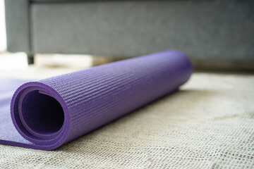 Rolled purple yoga exercise mat on the floor in living room.
