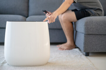 Unrecognizable Asian young man using and controlling a modern air purifier.