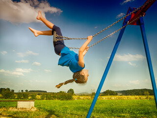 Upside down girl swinging on a swing in a playground, Poland
