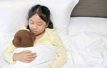 Sweet little girl is sleeping with a teddy bear in her bed at home,