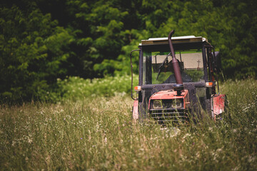 Naklejka premium an old red tractor mowing the grass near the forest. use of agricultural machinery on the farm