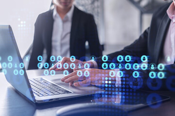 Two HR specialists in formal wear analyzing the recruitment market using laptop to boost the intern program at international consulting company. Social networking hologram icons.