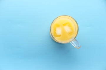 top view of a glass of orange juice with iece on blue background 