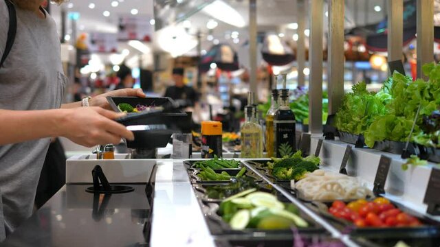 Female customer choosing salad at salad bar in supermarket
