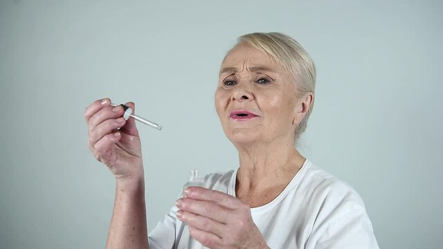 Happy attractive 70 years old woman applying serum or cosmetic oil on face