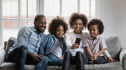 Happy millennial parents and children using smartphone for video or conference call. Black couple and kids talking to family members online or taking selfie together. Distance communication concept