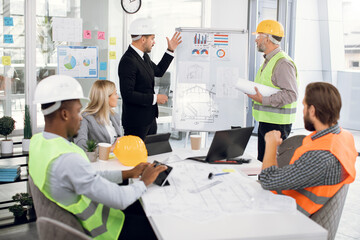 Young high-skilled bearded manager discussing the details of building project with experienced man...