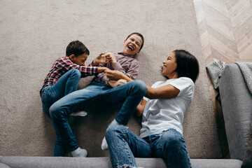 Happy african american family mom and two sons fooling around and having fun at home together. Top...