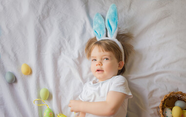 Cute funny baby with bunny ears and colorful Easter eggs at home on a white background