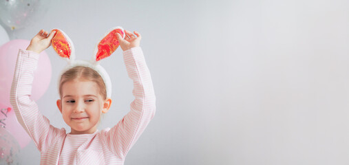 Cute little girl with bunny ears on Easter day. Happy child close-up on grey background with balloons at birthday party. Easter holiday concept. Happy birthday Banner. Copy space