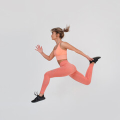 Athletic girl in a pink sports kit in a jump isolated on a gray background.