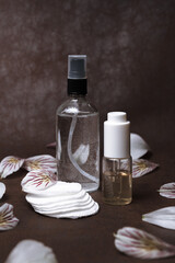 Fototapeta na wymiar Toner and facial oil serum in glass bottles arranged on table with cotton pads and flower petals showing concept of natural skin care treatment 