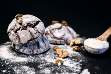 Chocolate crinkle cookies with powdered sugar icing. Homemade cracked chocolate ginger brownie biscuits on black background. Chocolate cookie with nuts, raisins and flour. Selective focus, copy space.