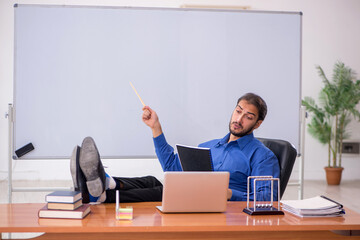 Young male teacher physicist sitting in the classroom