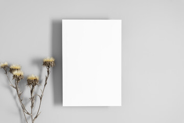 White paper empty blank, dried flowers on gray table. Invitation card mockup. Flat lay, top view, copy space, mockup