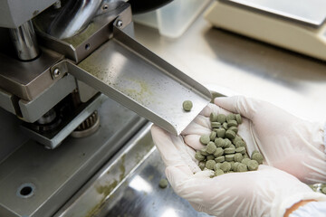 Pills in apothecary or 
pharmacist holding herbal medicine in hand from single punch tablet machine. Drugs industrail in laboratory background.