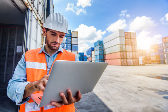 Confident Caucasian man engineer wearing white safety helmet using computer laptop and check for control loading containers box from Cargo freight ship for import and export, transport