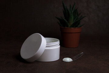 Opened cream jar and plastic spatula for daily skin care beauty treatment placed on table on dark background in studio 