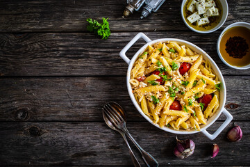 Roasted tomatoes with feta cheese and penne served in ceramic pan on wooden table