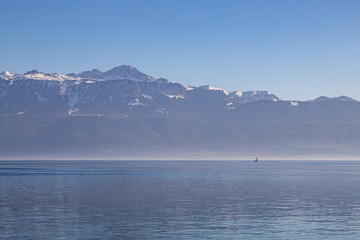 A boat on hazy, misty Lake Geneva and the Alps seen from Lausanne, Switzerland