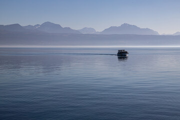 A boat on hazy, misty Lake Geneva and the Alps seen from Lausanne, Switzerland