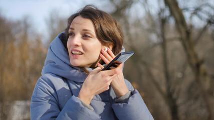 Young woman with wireless headphone is using her smartphone to send a voice message to a new social...