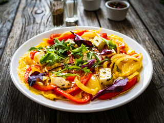 Delicious breakfast - scrambled eggs with onion, bell pepper, feta cheese and mix of young vegetable leaves on wooden table
