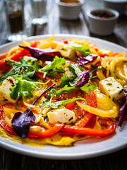 Delicious breakfast - scrambled eggs with onion, bell pepper, feta cheese and mix of young vegetable leaves on wooden table
