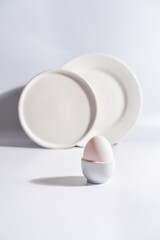 White egg with white plates, cup and alarm clock over white background for breakfast