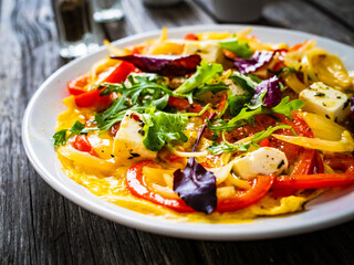 Delicious breakfast - scrambled eggs with onion, bell pepper, feta cheese and mix of young vegetable leaves on wooden table
