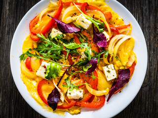 Delicious breakfast - scrambled eggs with onion, bell pepper, feta cheese and mix of young vegetable leaves on wooden table
