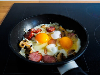 Breakfast - sunny side up eggs with sausages, champignon and onion in frying pan

