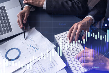 Two traders man and woman researching historic data to predict stock market behavior. Internet trading concept. Forex and financial hologram chart over the table with the documents