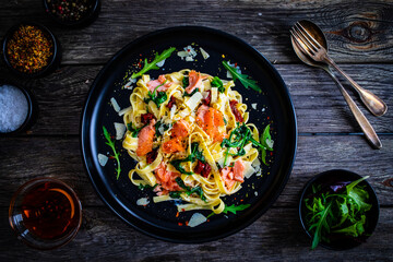 Tagliatelle with salmon nuggets, arugula and sun-dried tomatoes on wooden table
