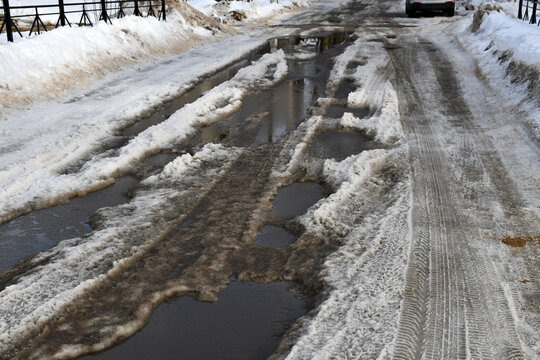 The beginning of spring or winter thaw. Roadway with large puddles and holes. Dirty ice and snow on the road.