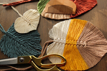Leaf macromes made of yellow, white, beige and turquoise colored threads, wooden comb and scissors on the wooden floor.