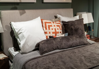 Close-up of new blanket with decorative pillows, wooden headboard in bedroom in sample model of house or apartment