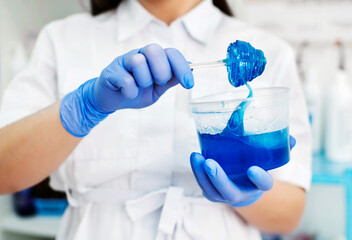 A girl beautician in a white coat holds blue sugar paste for epilation on a spatula in a beauty salon. Spatula and epilation paste in hand. Shugaring