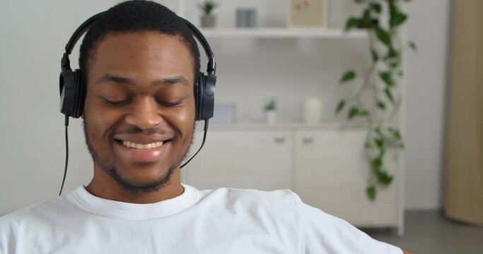 Afro american guy student businessman resting at home wears white shirt and headphones listens to his favorite music sings song enjoys melody great sound in new device concept of rest during lock down