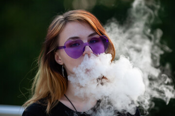 Vape teenager. Young pretty white caucasian girl in purple glasses on her head an electronic...