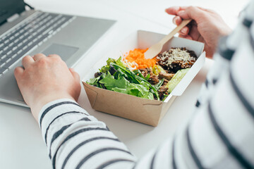 Woman having lunch in recycled bowl using laptop. Food delivery, quarantine, take out food concept